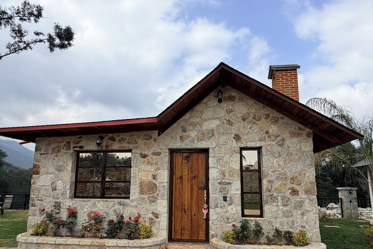 A stone house with a wooden door and windows, surrounded by a garden with flowers.