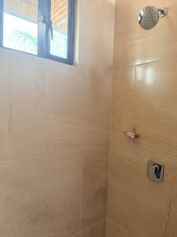 A bathroom with beige tiles, a showerhead, a towel rack, and a window with a view of palm trees.