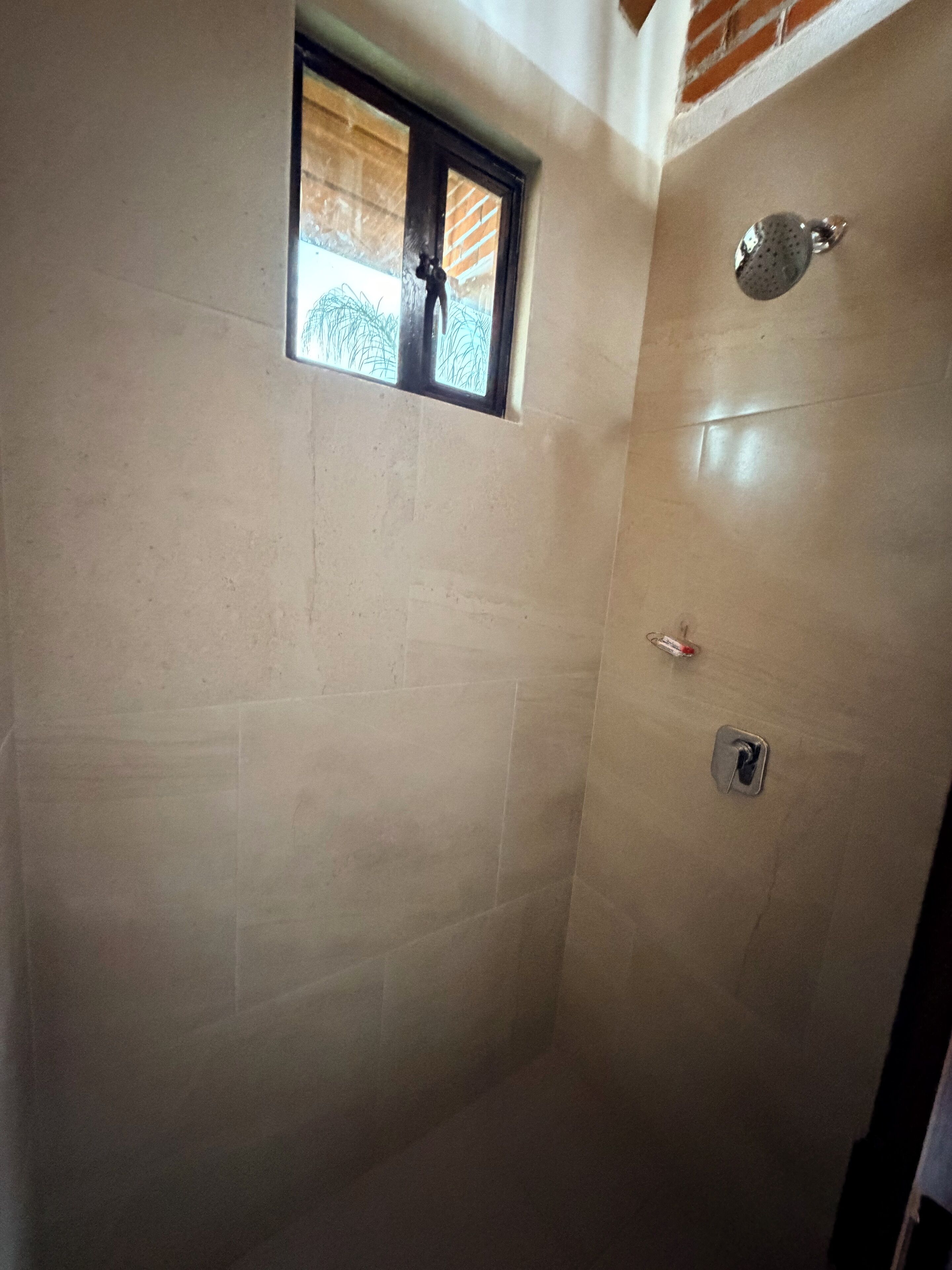 Un espacio de ducha con azulejos, una pequeña ventana y un cabezal de ducha.