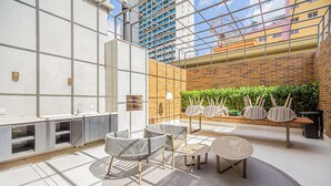 Un espacio interior moderno con techo alto, pared de ladrillo con plantas y zona de estar con mesas y sillas.