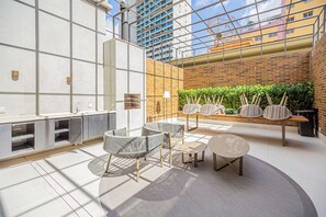 A modern indoor space with a high ceiling, a brick wall with greenery, and a seating area with tables and chairs. - Flat c/ Piscina e Academia na Chácara Klabin (São Paulo)