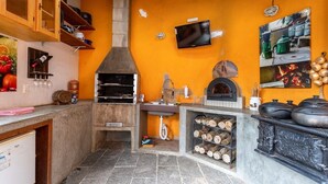 A kitchen with a wood-fired oven, a television mounted on the wall, and a tiled backsplash. - Casa com fogão a lenha para 7 | Vale das Videiras (Itaipava, Petropolis)