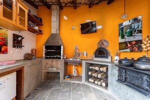A kitchen with a wood-fired oven, a television mounted on the wall, and a tiled backsplash. - Casa com fogão a lenha para 7 | Vale das Videiras (Itaipava, Petropolis)