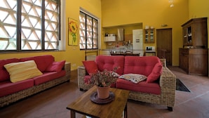 A spacious living area with a red sofa, a wicker couch, and a wooden coffee table. A kitchen with modern appliances is visible in the background. - The Colletalli Barn (Radicondoli)