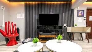 Ein modernes Wohnzimmer mit Fernseher, zwei weißen runden Tischen, einem roten Sessel, einer Couch und einer hölzernen Bank.