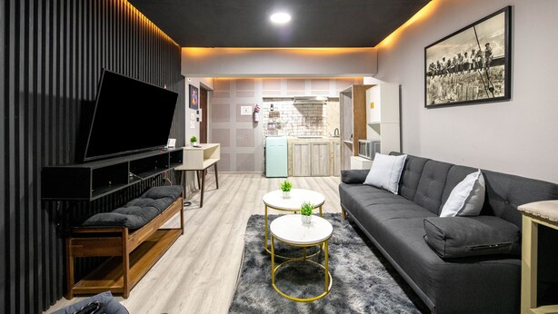 Ein modernes Wohnzimmer mit einer Couch, zwei Couchtischen, einem Fernseher und einer Küche im Hintergrund.