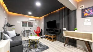 Ein modernes Wohnzimmer mit einer Couch, einem Esstisch, einem roten Sessel, einem Fernseher und einer kleinen Pflanze.