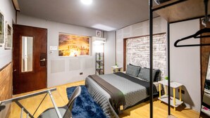 Ein Schlafzimmer mit Etagenbett, einem Stadtbildgemälde, einer Ziegelwand und einer Holztür sowie einem kleinen weißen Tisch.