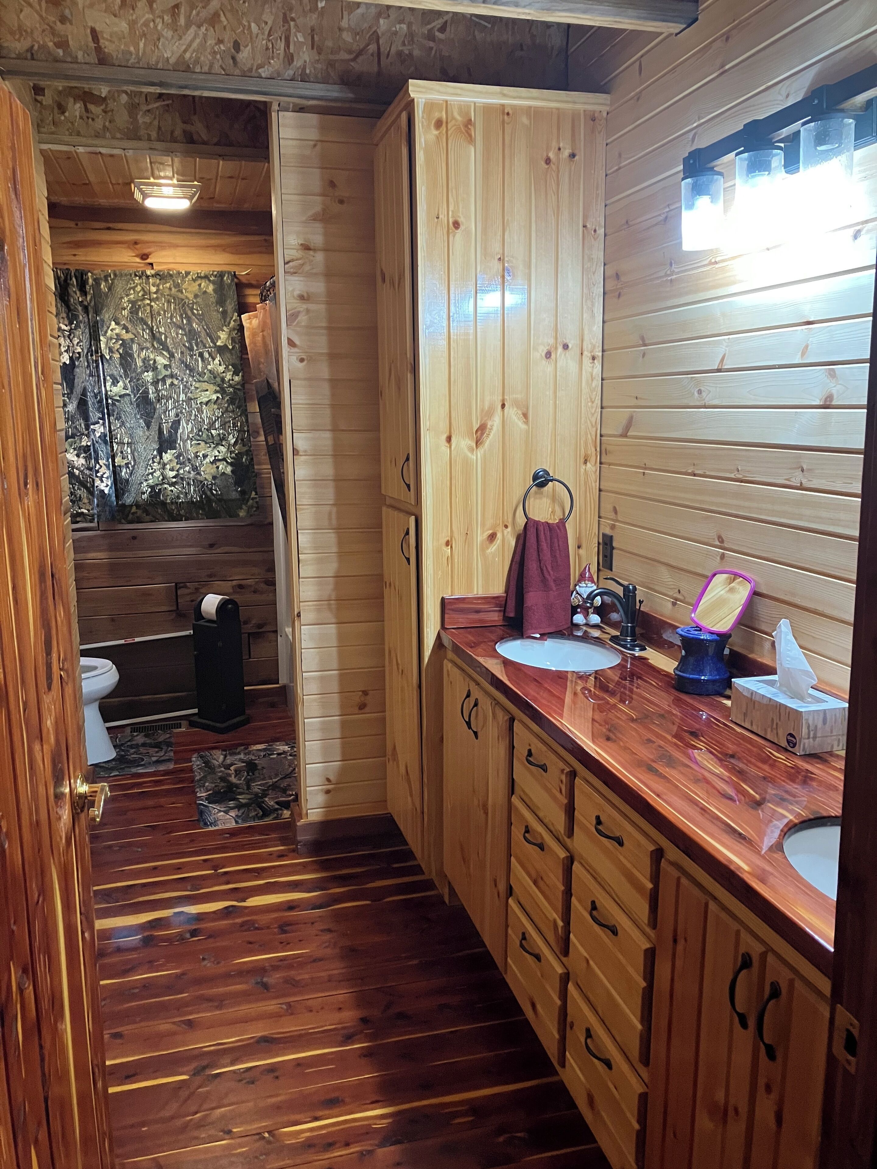 A wooden cabin bathroom with a toilet, sink, and cabinets.