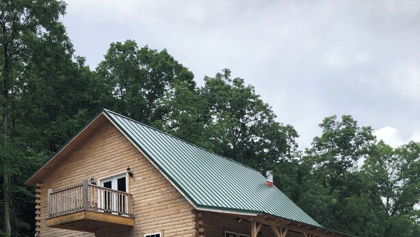 Eine Blockhütte mit Balkon und überdachter Veranda, umgeben von Kies und Bäumen.