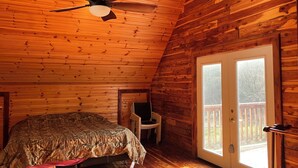 Ein Schlafzimmer in einer Blockhütte mit einem Bett, einem Deckenventilator und einem großen Fenster.
