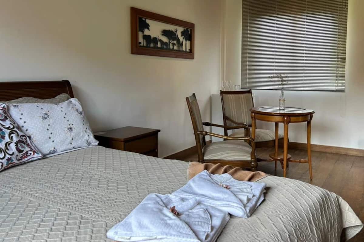 Una cama bien hecha con una manta estampada, una silla, una mesita con una botella y una chimenea en una habitación de hotel.