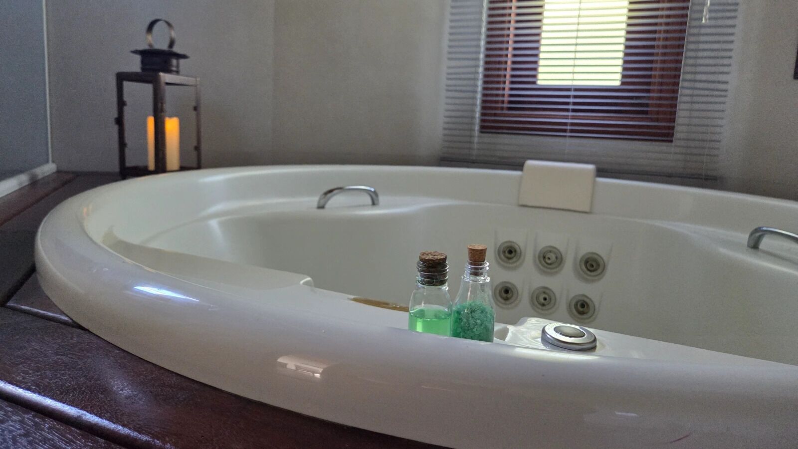 A white bathtub with a faucet, two bottles of bath salts, and a candle in a lantern.
