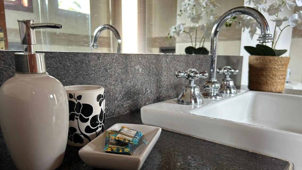 Un baño con lavamanos blanco, encimera de mármol, dispensador de jabón, jabonera y una taza decorativa.