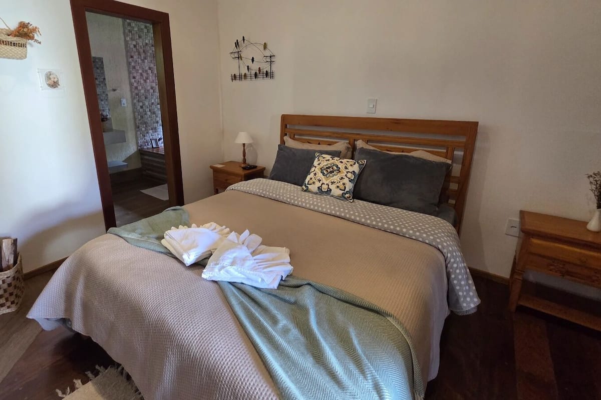 Una cama bien hecha con cabecera de madera, una mesita de noche con lámpara y una obra de arte colgada en la pared.