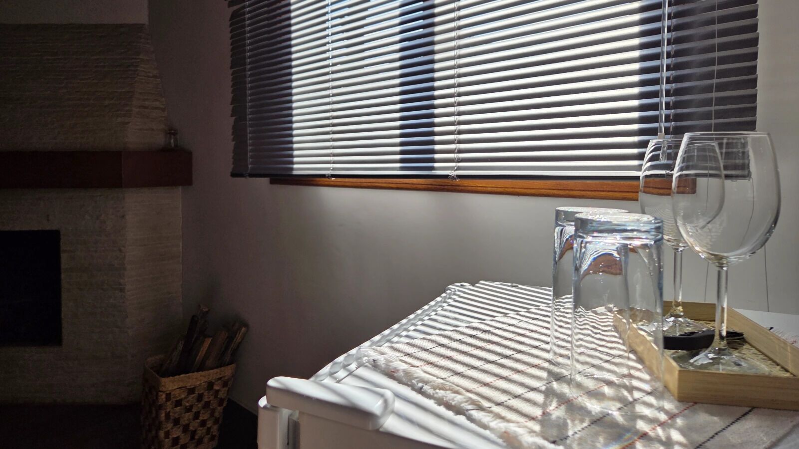 A kitchen with a white countertop, a window with blinds, and a basket of utensils.