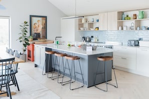 Een moderne keuken met een centraal eiland, barstoelen en een eethoek met een tafel en stoelen.