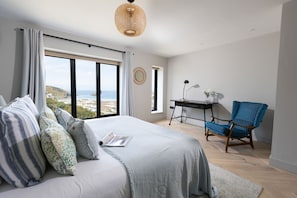 Een slaapkamer met een groot bed, een bureau, een stoel en uitzicht op zee.