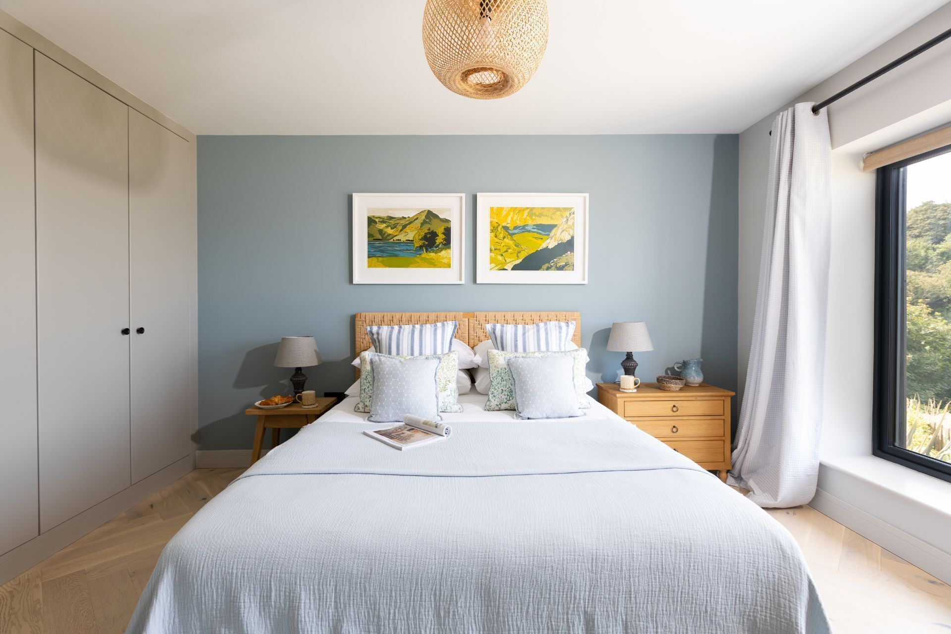 A bedroom with a large bed, two bedside tables, a wooden headboard, and two framed landscape paintings.