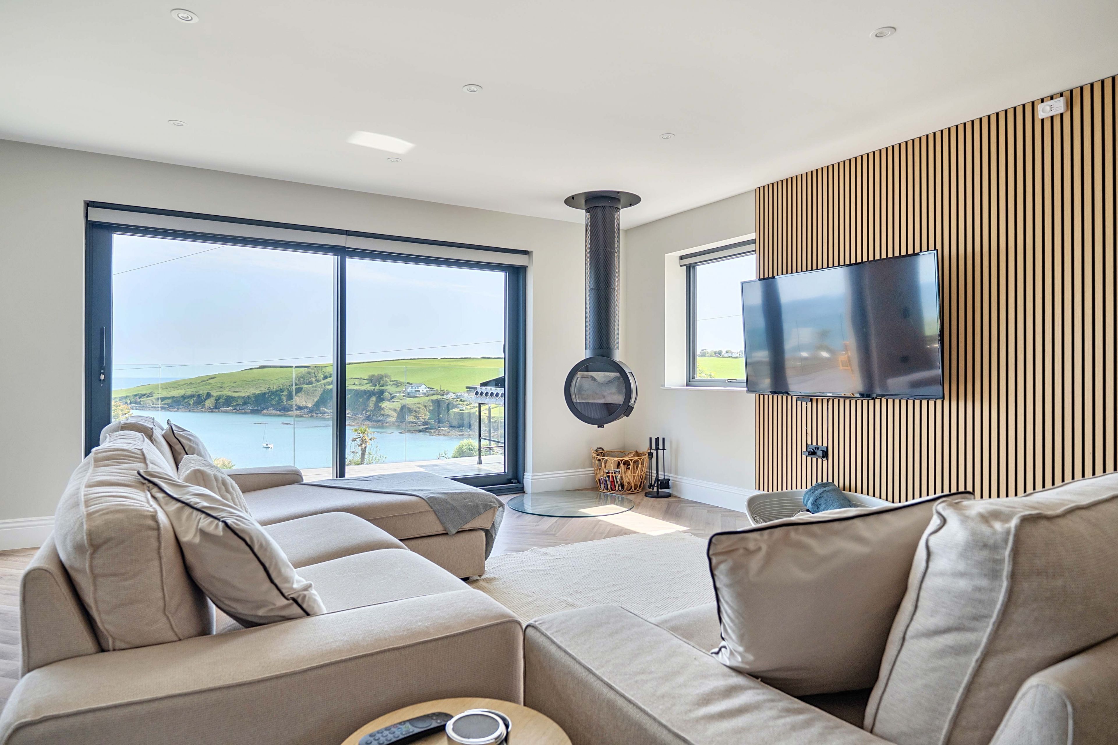 A modern living room with a sofa, a television, and a view of the sea.
