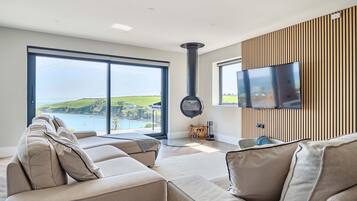 A modern living room with a sofa, a television, and a view of the sea.