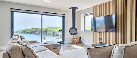 Una sala de estar moderna con un sofá, un televisor y vista al mar.