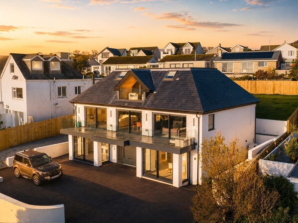 Une maison moderne à deux étages, dotée d’un balcon, d’une allée et d’une voiture garée.