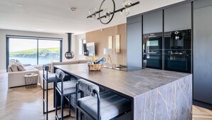 A modern kitchen with a marble island, bar stools, a large window with a view, and built-in appliances.