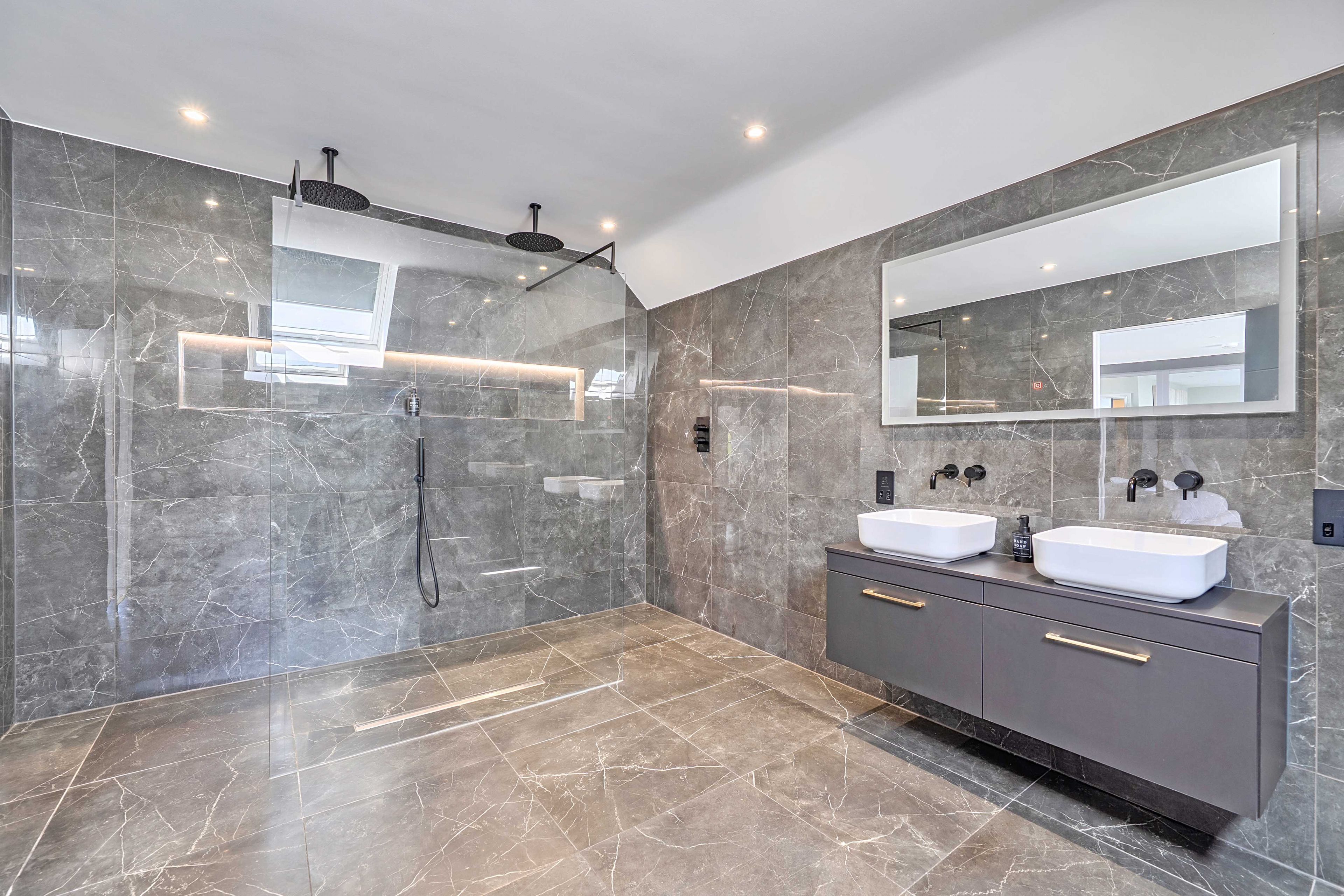 A modern bathroom with a walk-in shower, a large mirror, and a vanity with two sinks.