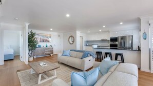 A modern living room with a sofa set, a coffee table, and a kitchen area with a refrigerator and microwave. - Bargara Coastal Escape – Modern 3 Bedroom Penthouse with Sea Views (Bargara)