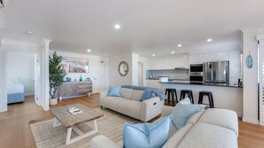 Ein modernes Wohnzimmer mit einer Sofagarnitur, einem Couchtisch und einer Küchenzeile mit Kühlschrank und Mikrowelle.