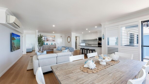 A modern living room with a dining area, a kitchen, and a view of the sea. - Bargara Coastal Escape – Modern 3 Bedroom Penthouse with Sea Views (Bargara)