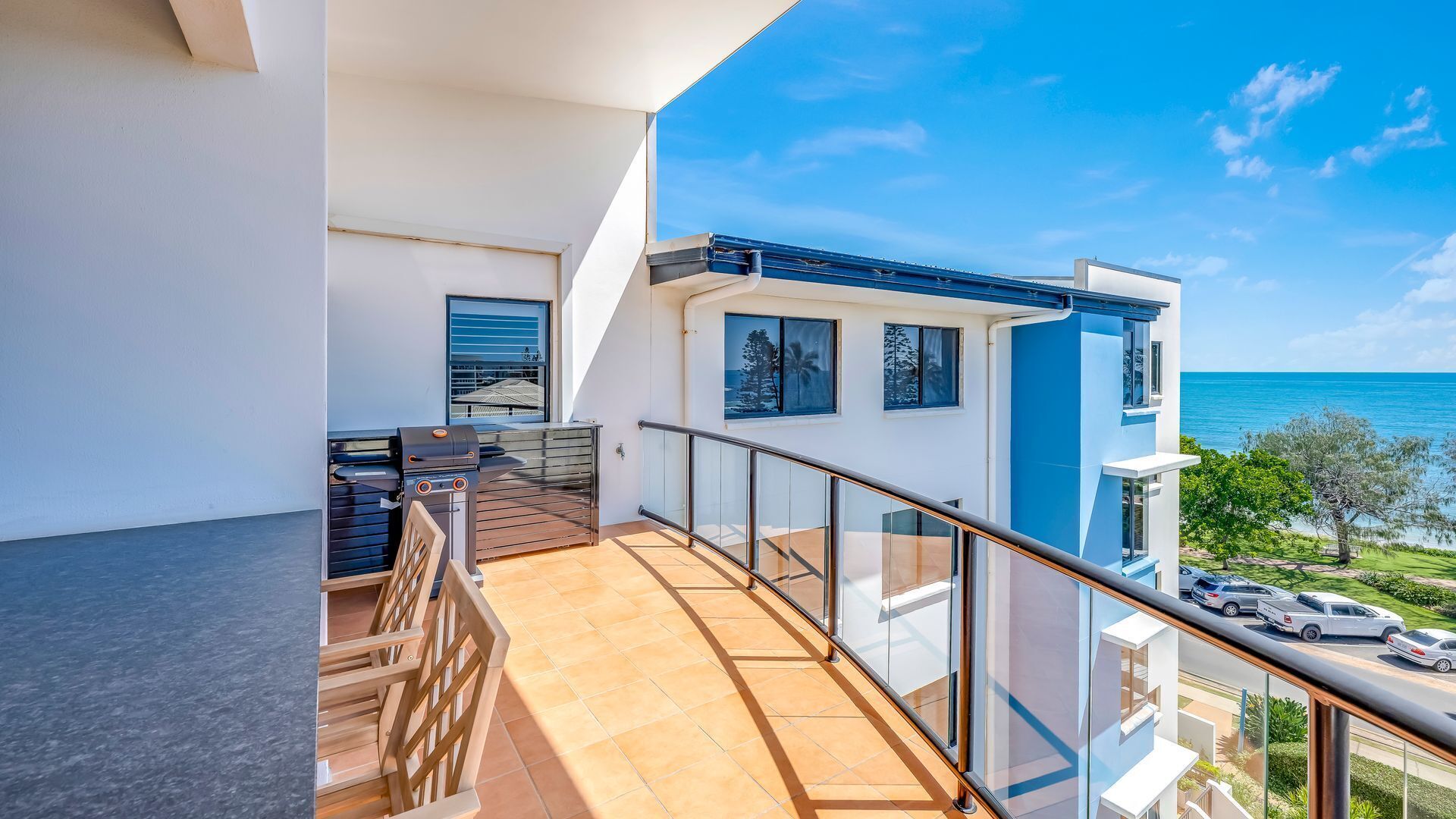 Un balcone con vista sull'oceano, un barbecue e un parapetto in vetro.