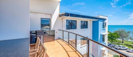 Un balcone con vista sull'oceano, un barbecue e un parapetto in vetro.