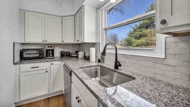 A kitchen with white cabinets, a granite countertop, a stainless steel sink, a built-in microwave, and a window with a view of trees.