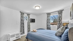 A bedroom with a bed, a TV mounted on the wall, and a window with curtains.