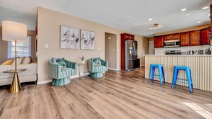 Eine moderne Küche mit Holzboden, einer zentralen Kochinsel mit Barhocker und einem Essbereich mit Sofa und Stühlen.