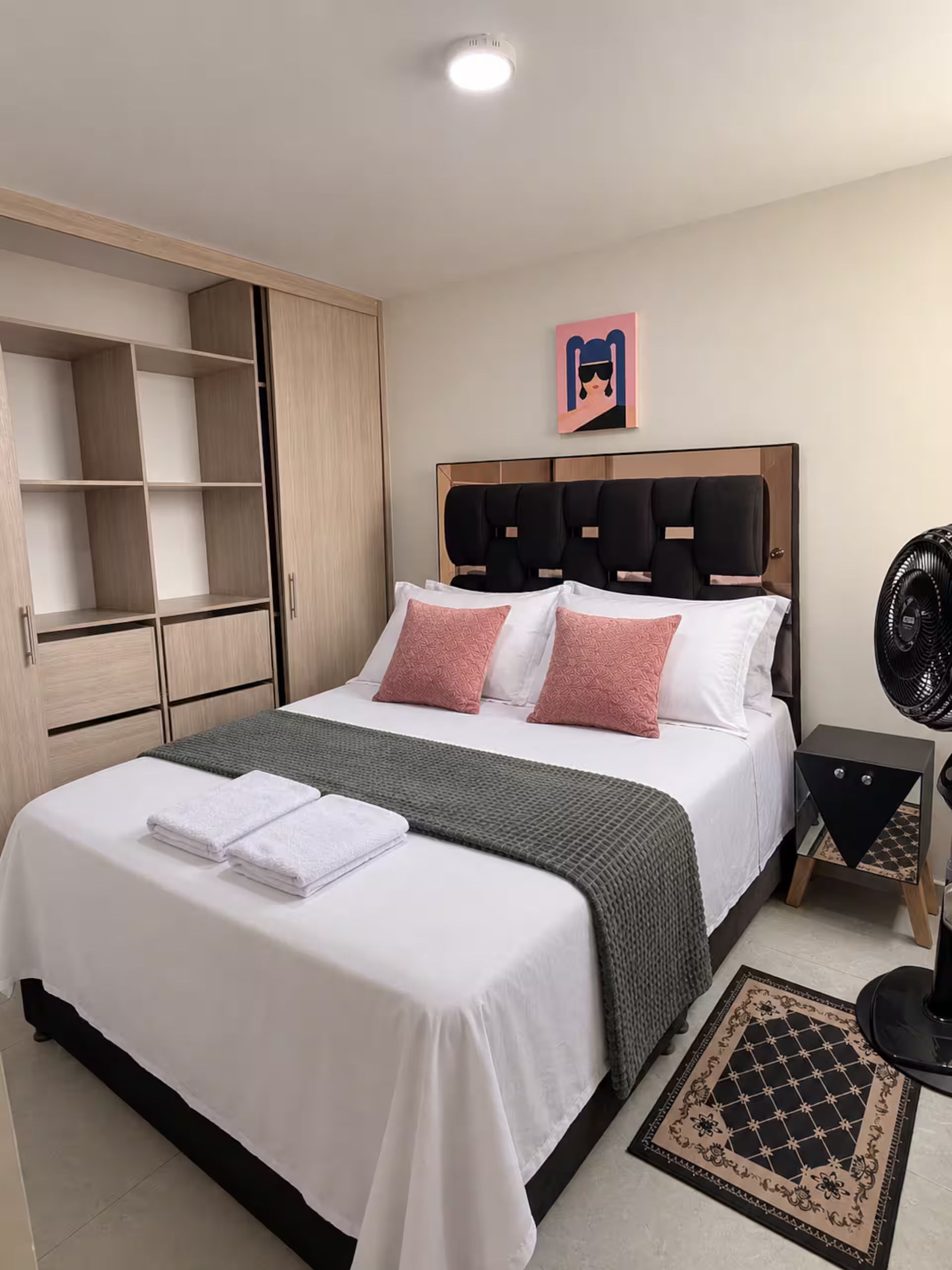 Una habitación de hotel con cama, armario, mesita de noche y lámpara de pie.
