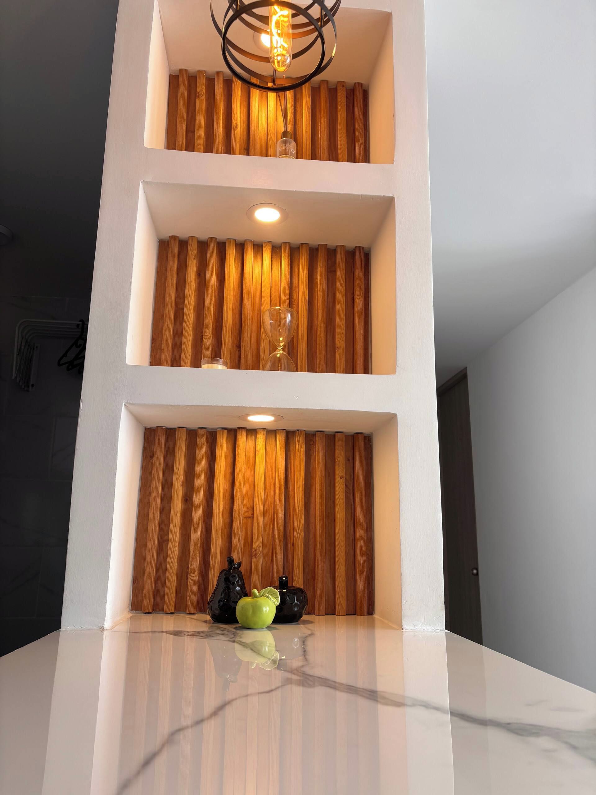 Un interior moderno con encimera de mármol, listones de madera en la pared y una lámpara colgante.