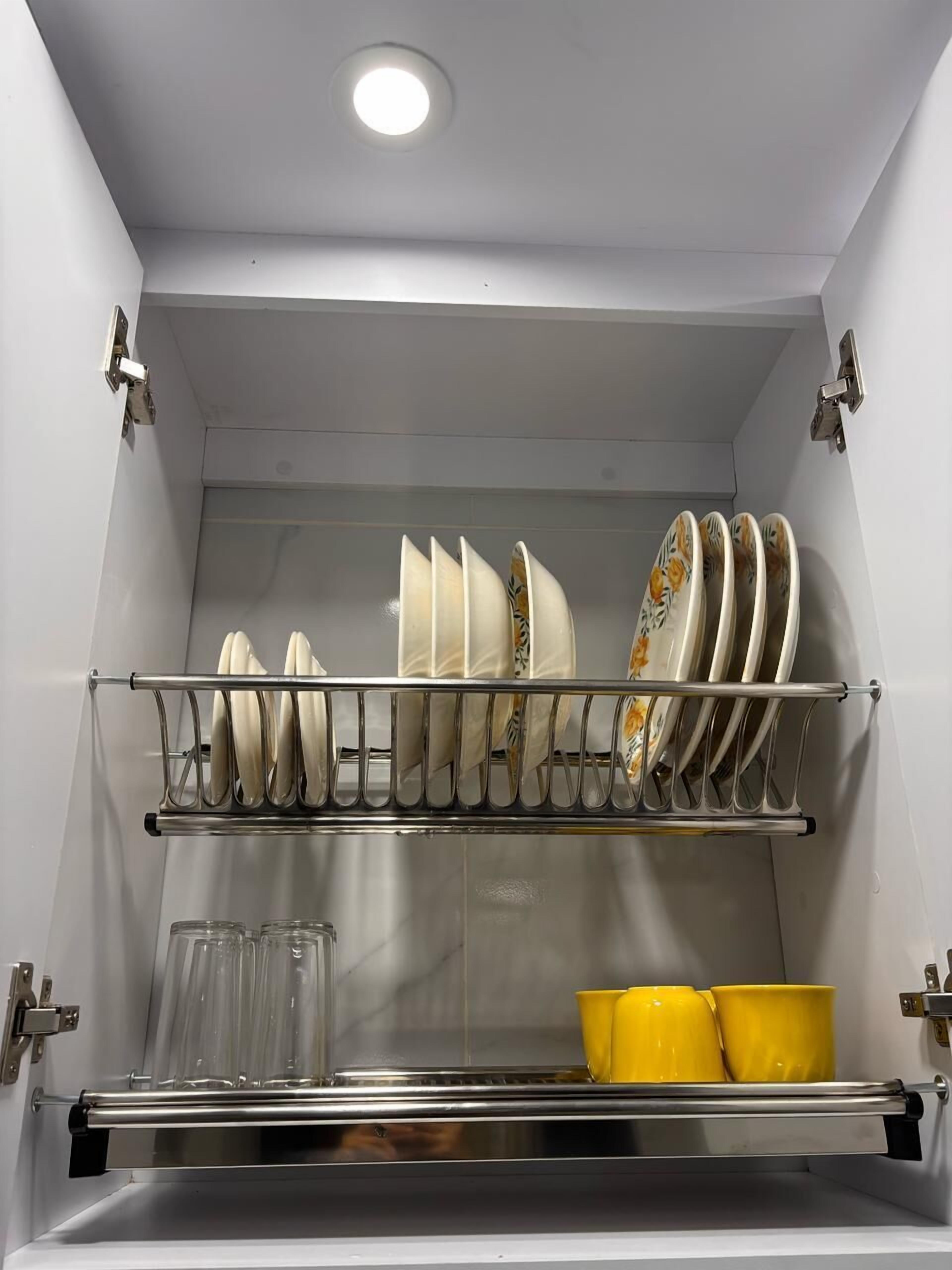 Eine Küche mit Geschirrregal, das Teller und Schüsseln hält, einem Glasregal mit Tassen und einem Edelstahlbackofen.