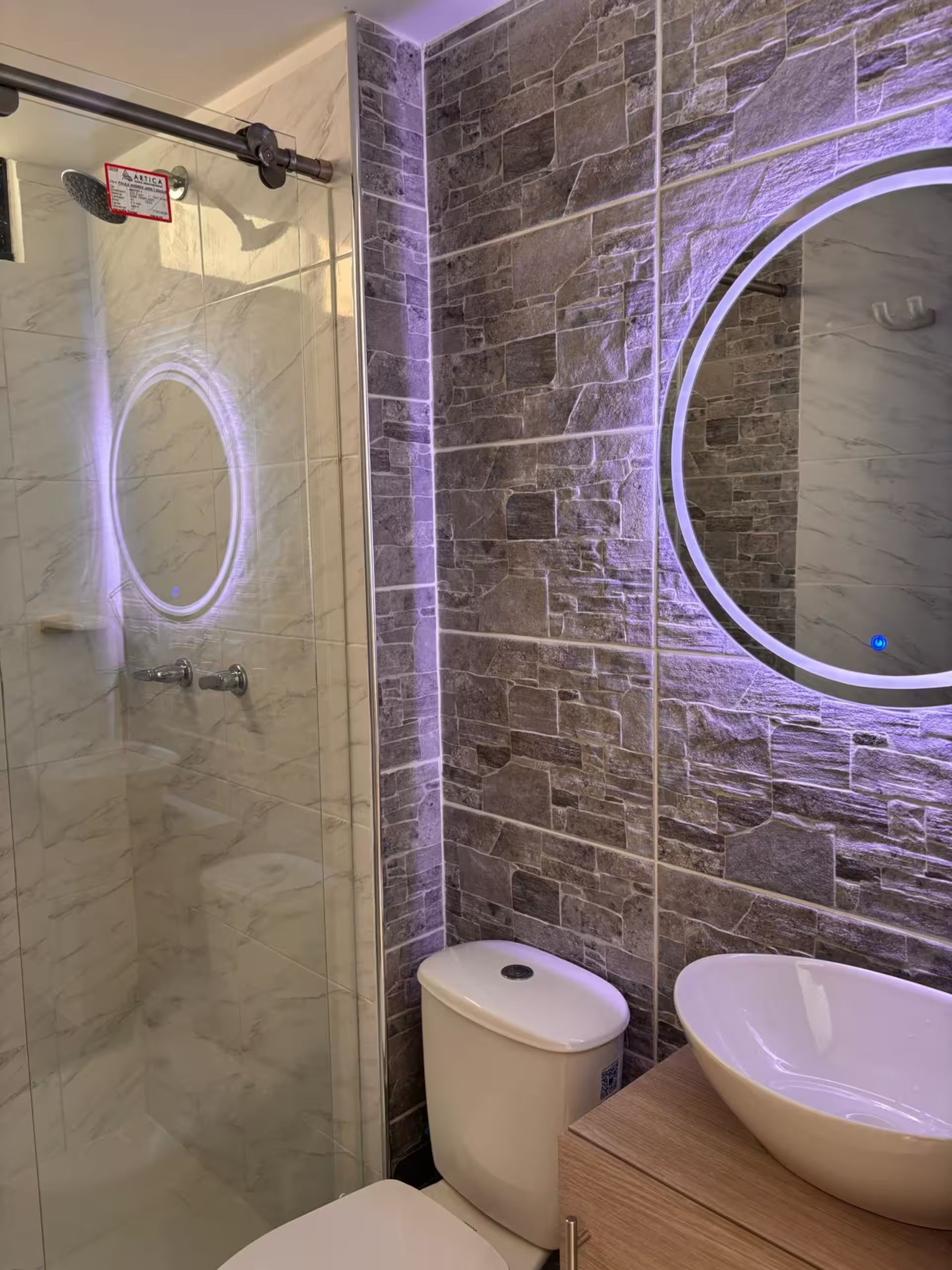 Un baño con cabina de ducha de vidrio, inodoro y tocador con lavamanos.