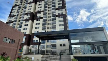 Un edificio residencial de gran altura con un diseño moderno, que cuenta con un acceso cubierto y un logotipo visible.