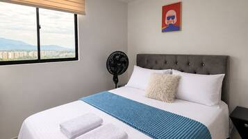 Una habitación de hotel con cama, ventana, ventilador y vista a la ciudad.