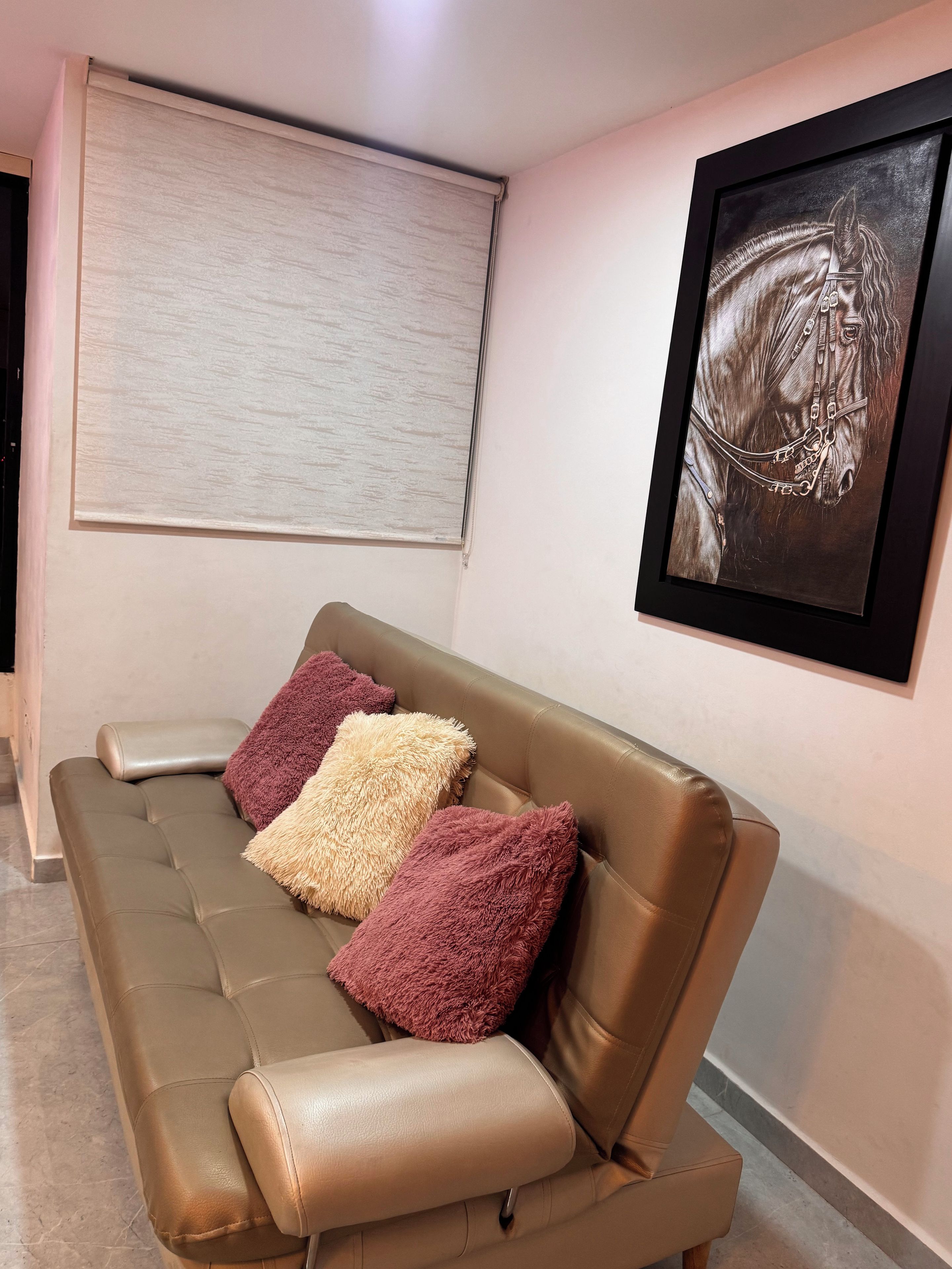 A room with a brown leather sofa, a large window with blinds, and a framed artwork on the wall.