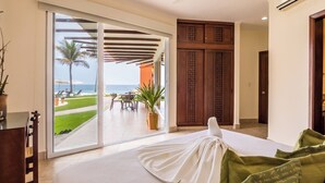 A hotel room with a large sliding glass door leading to a patio with a view of the ocean and palm trees.