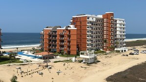 A multi-story hotel with balconies, a pool area, and a beach view.