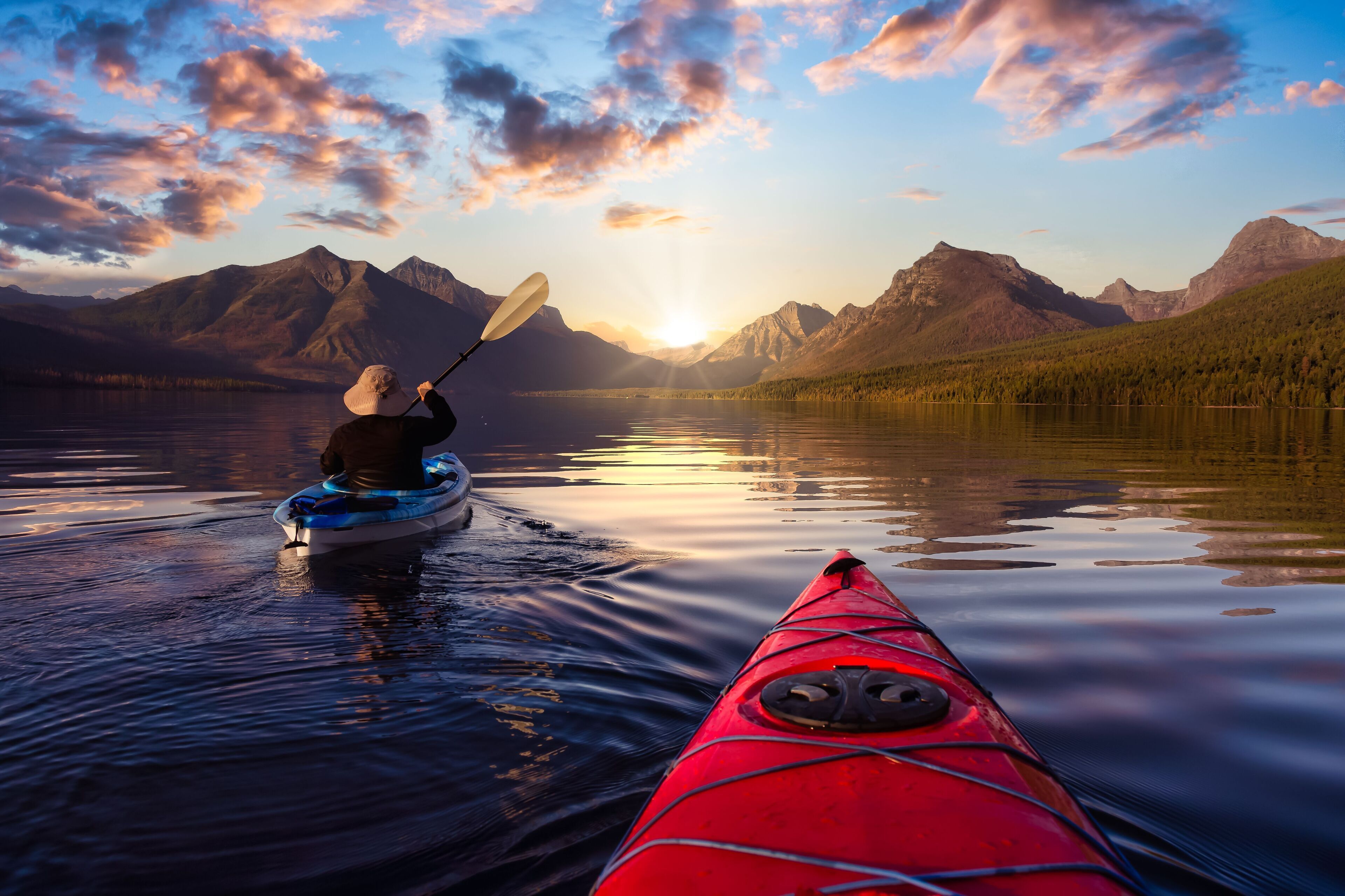 A kayaker in a red kayak on a calm lake with mountains in the background.