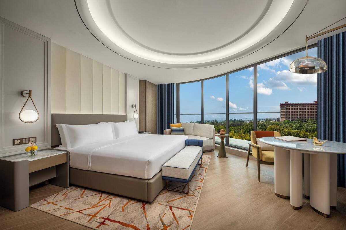 Une chambre d’hôtel moderne dotée d’un grand lit, d’un coin salon, d’une table à manger et offrant une vue sur la ville.