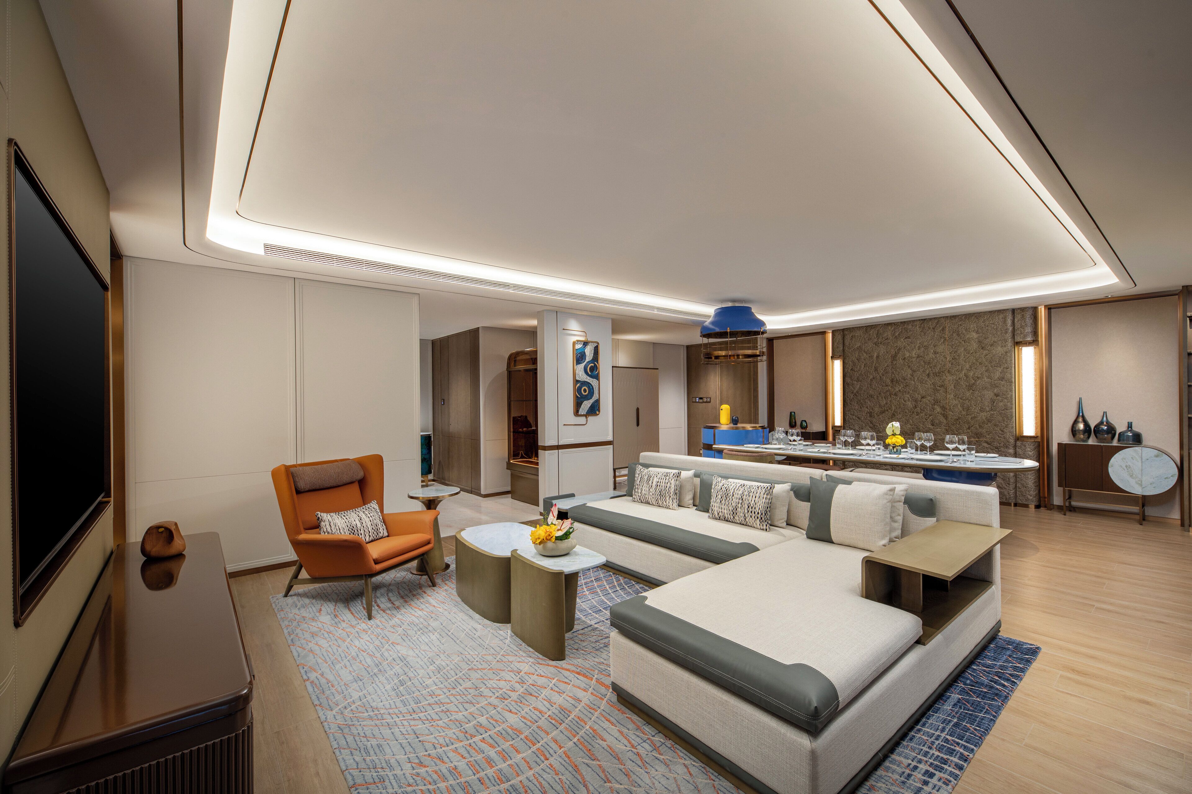 A modern hotel room with a large bed, a sofa, a dining area, and a TV.