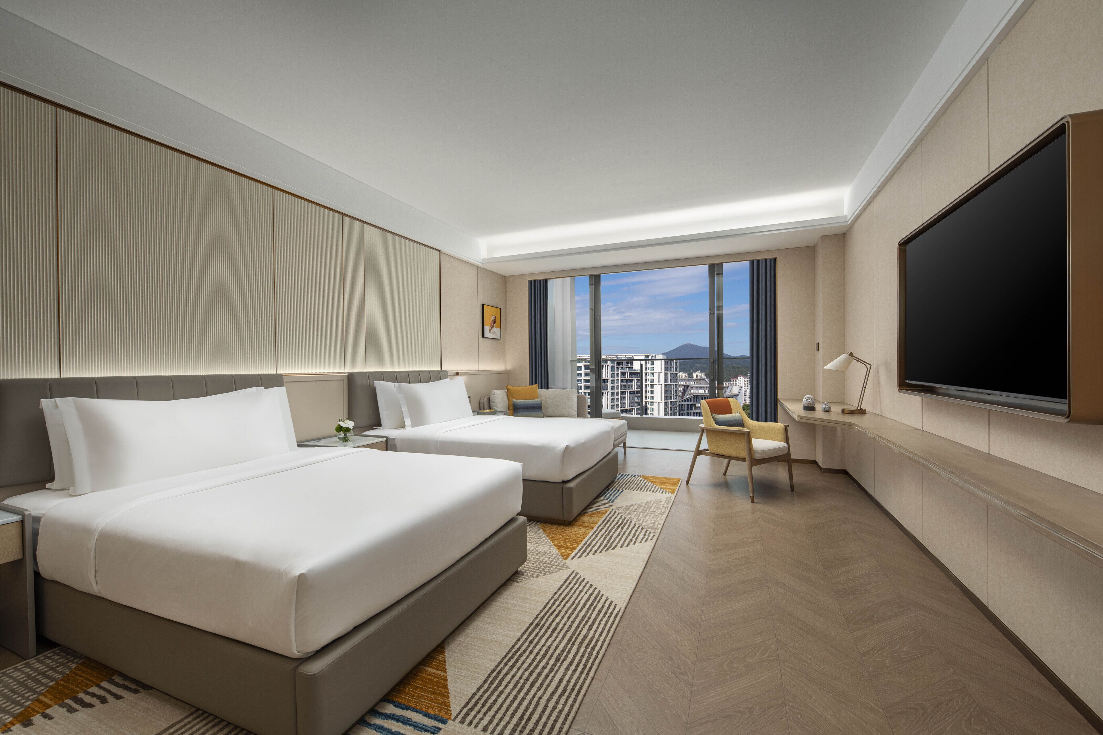 A modern hotel room with two beds, a TV, a desk, and a large window with a city view.